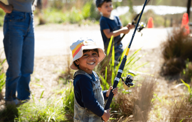 Child smiling holding a fishing rod at the creek