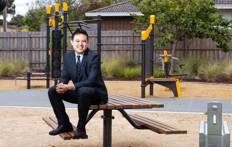 A man in a suit sits on a picnic table in front of play equipment