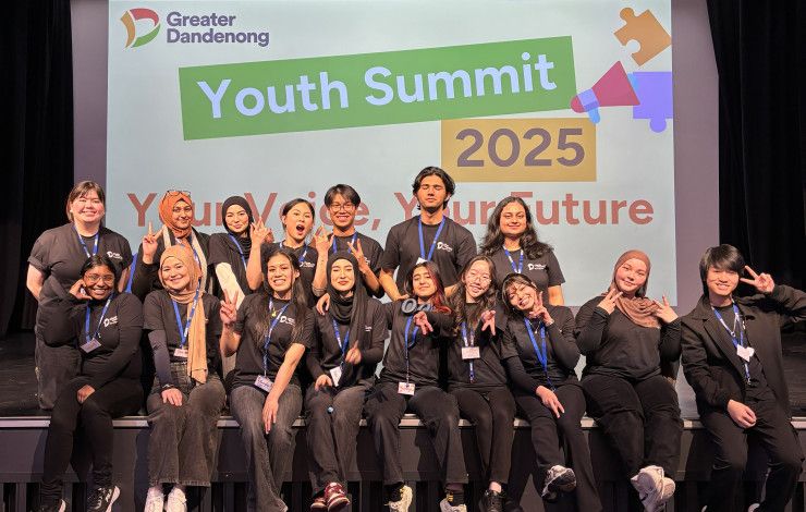 A large group of young people pose together on a stage in front of a sign that reads Youth Summit 2025