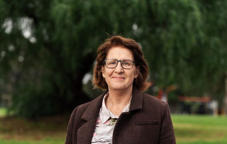A smiling woman stands in a park.