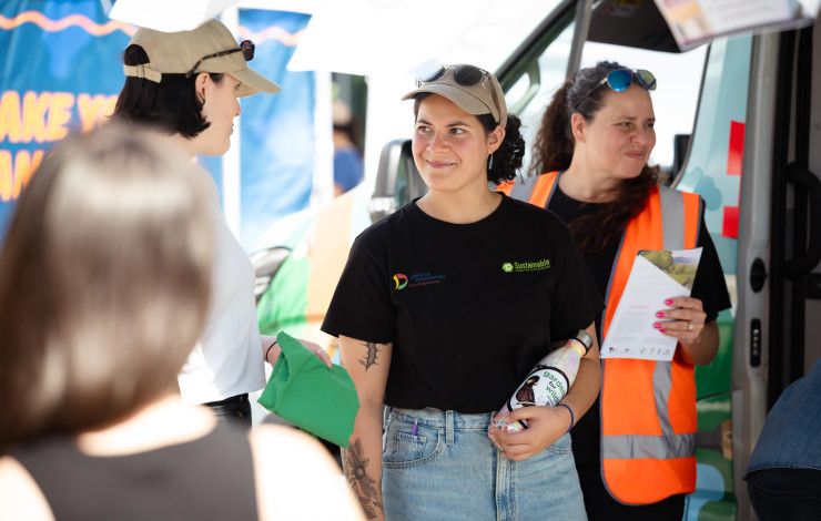 A woman wearing a black t-shirt and khaki cap smiles to a woman standing beside her.