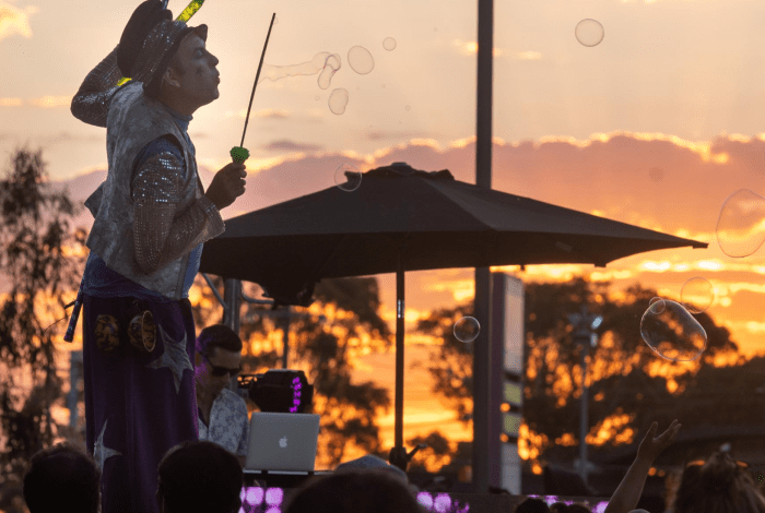 a stilt walker standing above a crowd blowing large bubbles