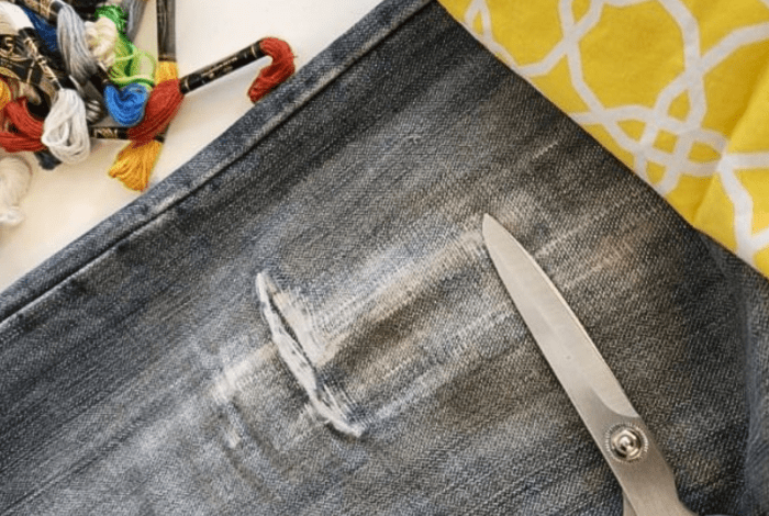 A torn pair of jeans with scissors, yellow fabric and coloured embroidery threads.