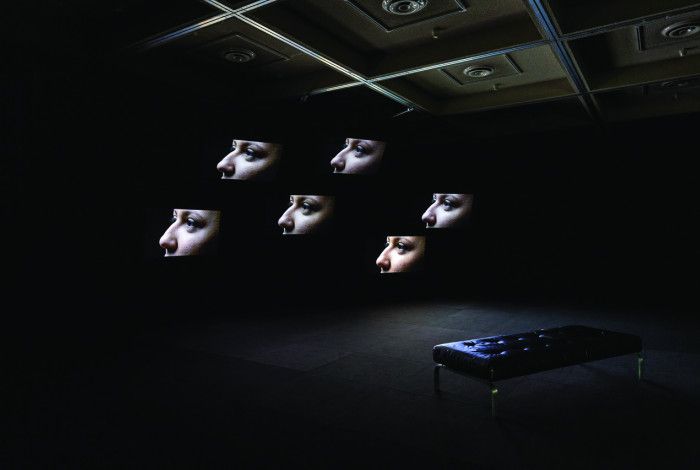  Installation view  of Vernon Ah Kee's work, Lullaby, featuring 6 profiles of faces displayed on screens in a darkened room