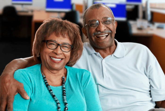 A man with his arm around a womans shoulders, both smiling at the camera.