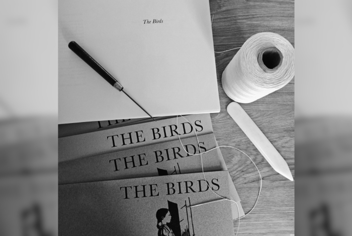 Assorted objects on a table; awl, bone folder, waxed thread