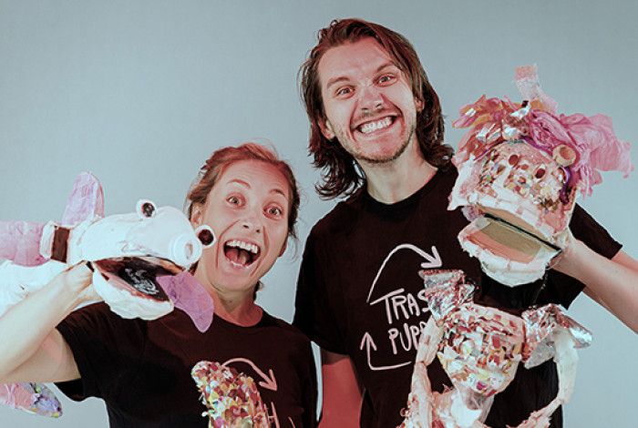 Two individuals behind toy rubbish bins, using cardboard puppets