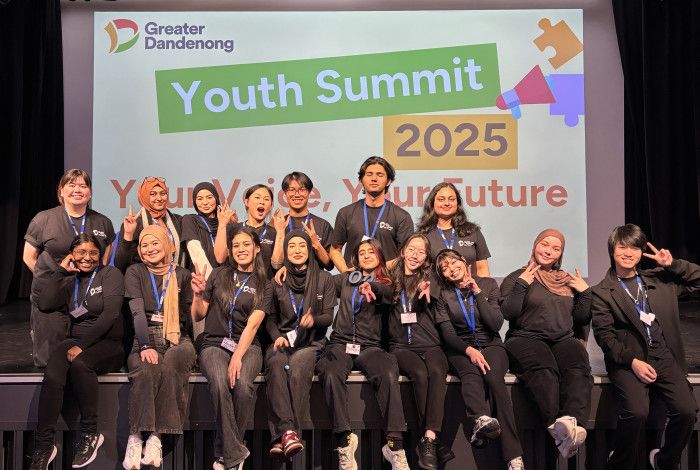 A large group of young people pose together on a stage in front of a sign that reads Youth Summit 2025