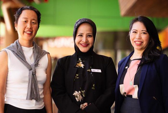 Three women stand in a line and smile at the camera