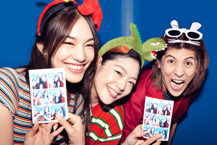 Three women smiling and holding photos taken in a photobooth.