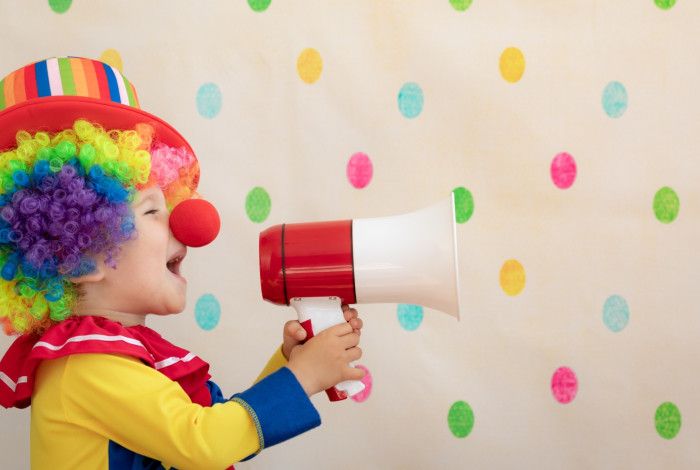 A child dressed as a clown yelling into a megaphone.