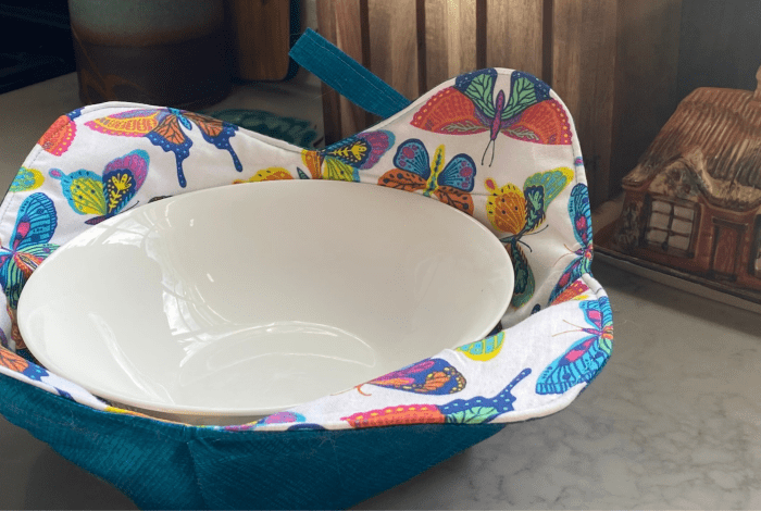 A white bowl in a colourful fabric bowl cosy next to a little china house model. 
