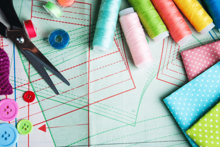 A collection of buttons, threads, fabrics and scissors laid out on sewing patterns. 
