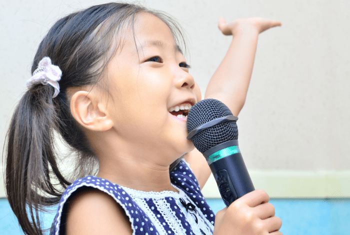 A child holding a microphone with one hand raised. 