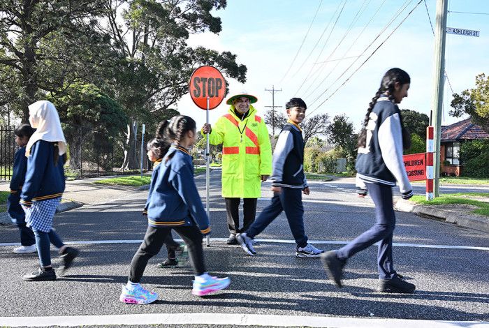 A man with a stop sign and children using a crossing