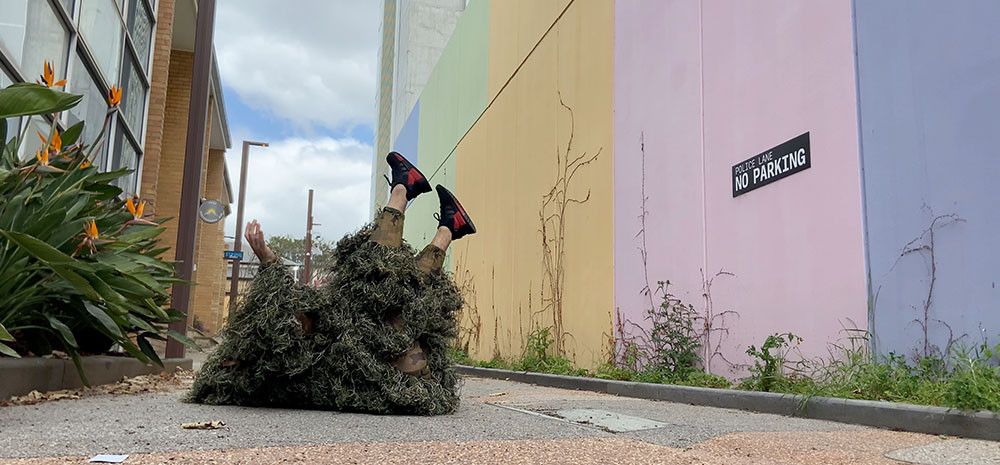 Person in shaggy grass like costume lying on their back in a public lane way
