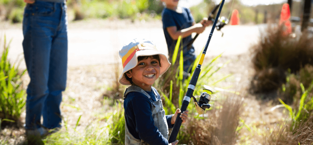 Child smiling holding a fishing rod at the creek