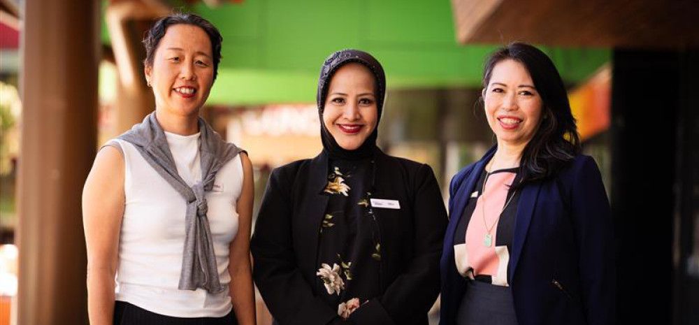 Three women stand in a line and smile at the camera