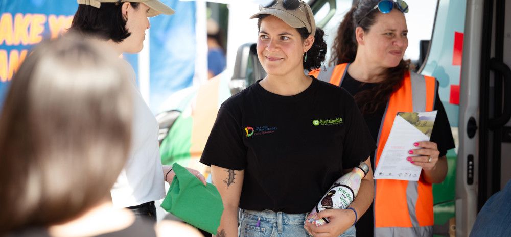 A woman wearing a black t-shirt and khaki cap smiles to a woman standing beside her.