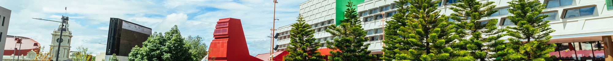 A stand of trees in front of a large civic building with a cloudy blue sky overhead.