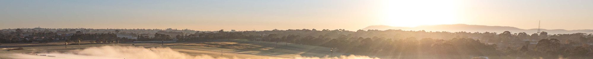Looking down over the home straight of a racing track that is covered in mist as the sun rises.
