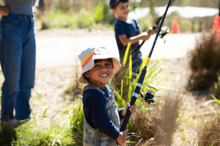 Child smiling holding a fishing rod at the creek