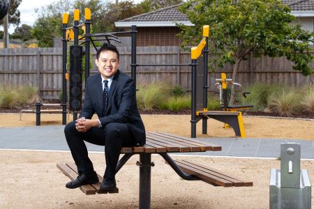 A man in a suit sits on a picnic table in front of play equipment