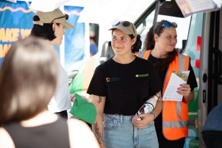 A woman wearing a black t-shirt and khaki cap smiles to a woman standing beside her.