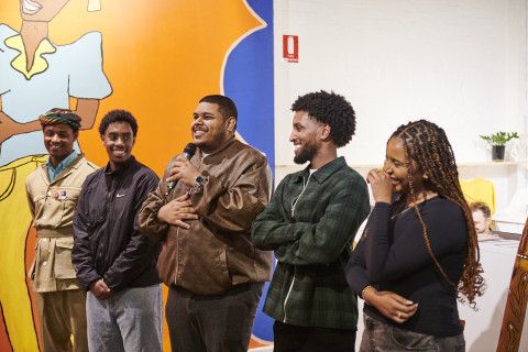 Five people stand in a row talking into a microphone