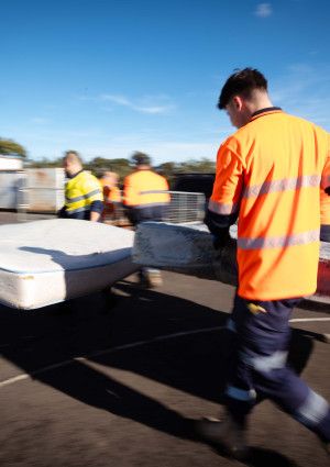 People in hi-vis carrying a mattress